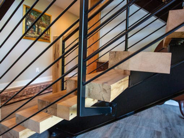 close up of light-colored wood stairs with black metal railing