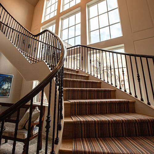 grand curved staircase with striped carpet and metal railings